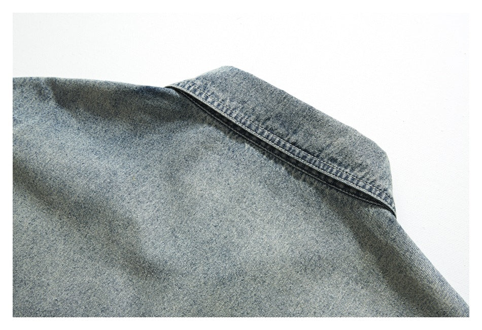 Close-up of the folded collar and double stitching on a faded blue denim jacket.
