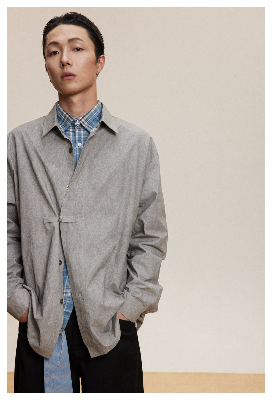Model wearing a gray collared button-front jacket over a blue plaid shirt and black trousers.