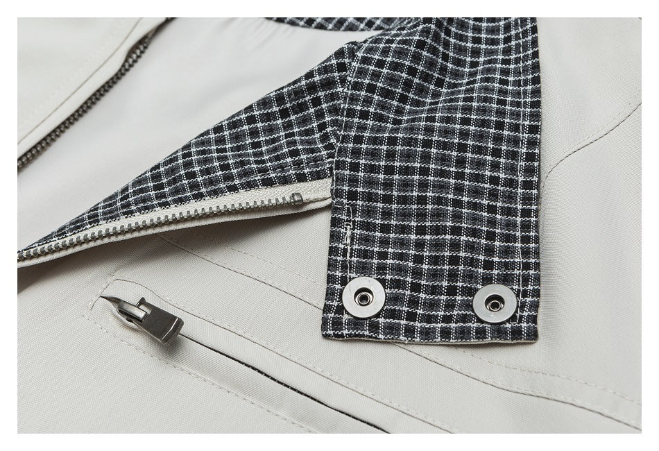Close-up of a light beige garment with black-and-white plaid trim, a metal zipper and two snap fasteners.
