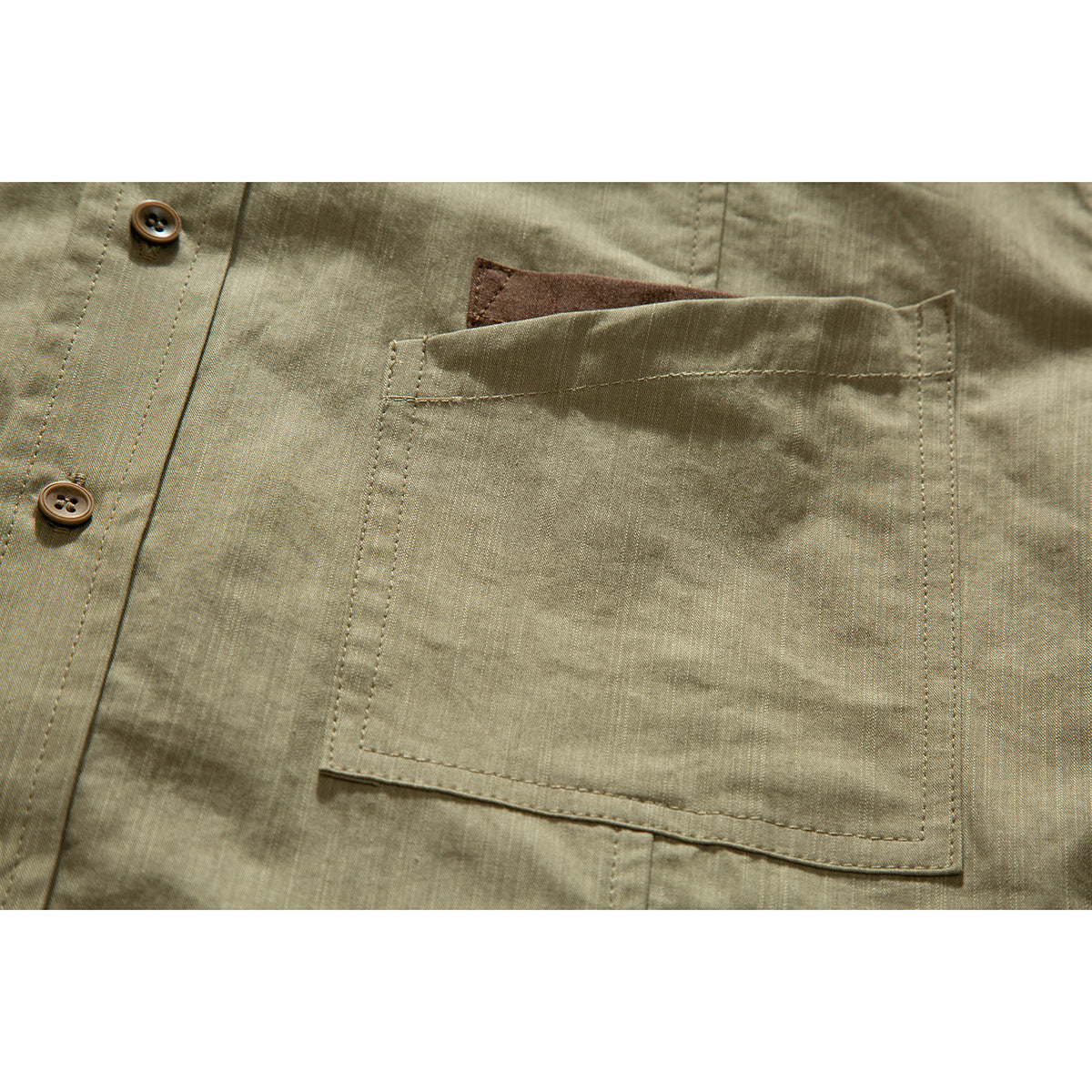 Close-up of an olive shirt's large stitched chest pocket with a brown fabric accent peeking above it.