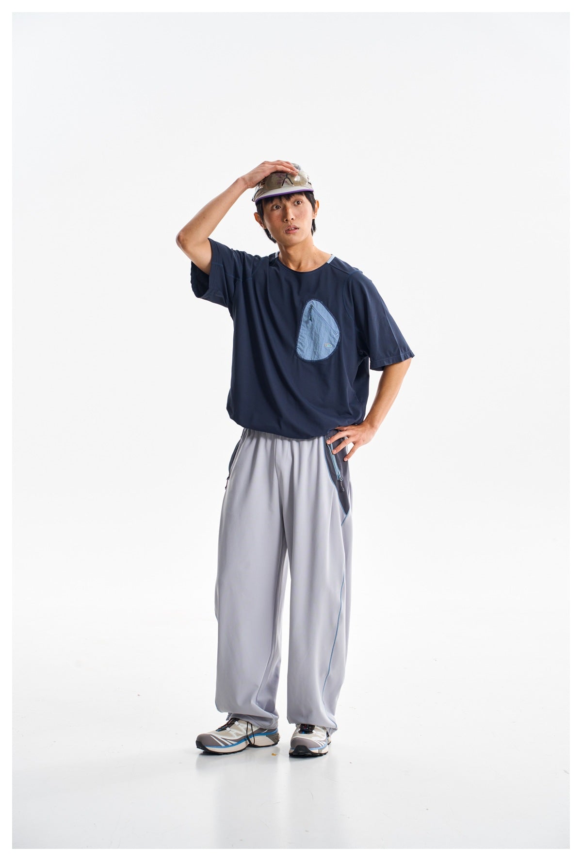 Model wearing a navy short-sleeve shirt with a light blue chest pocket and loose light gray pants.