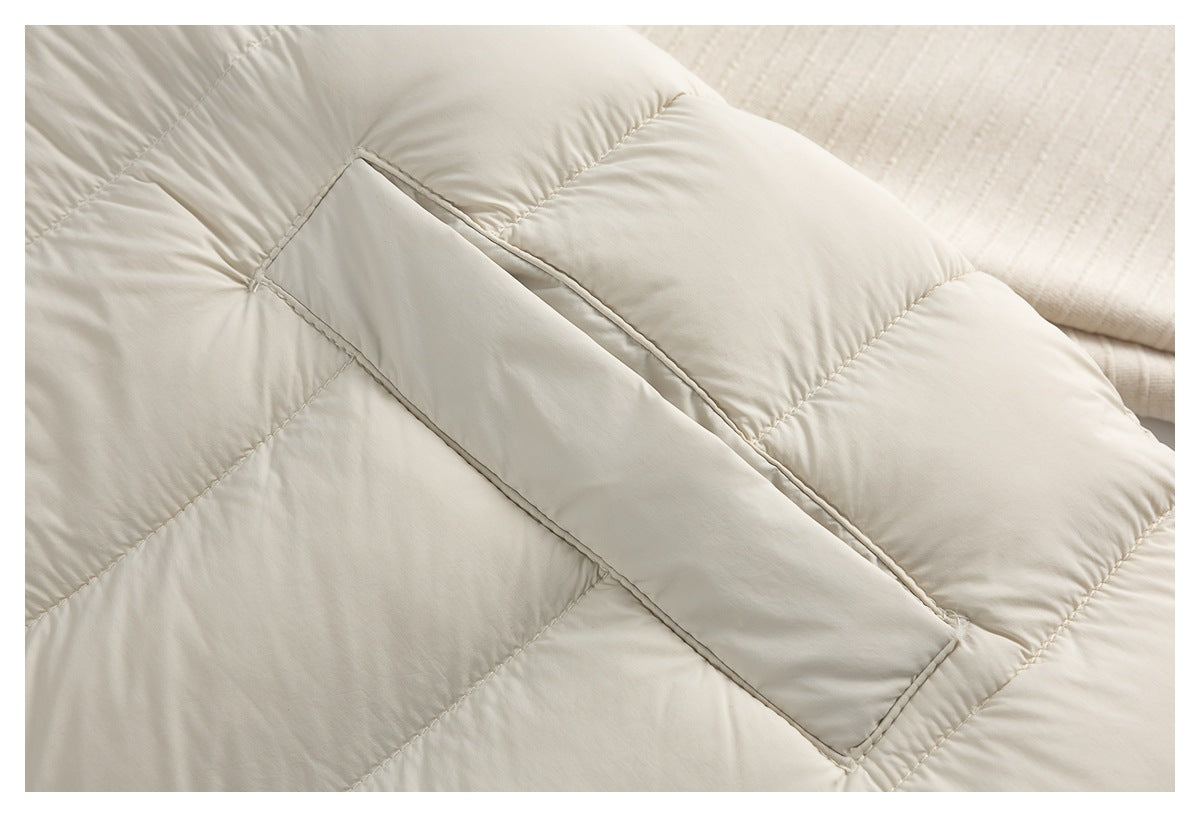 Close-up of a cream quilted vest showing a narrow welt pocket opening between padded panels.