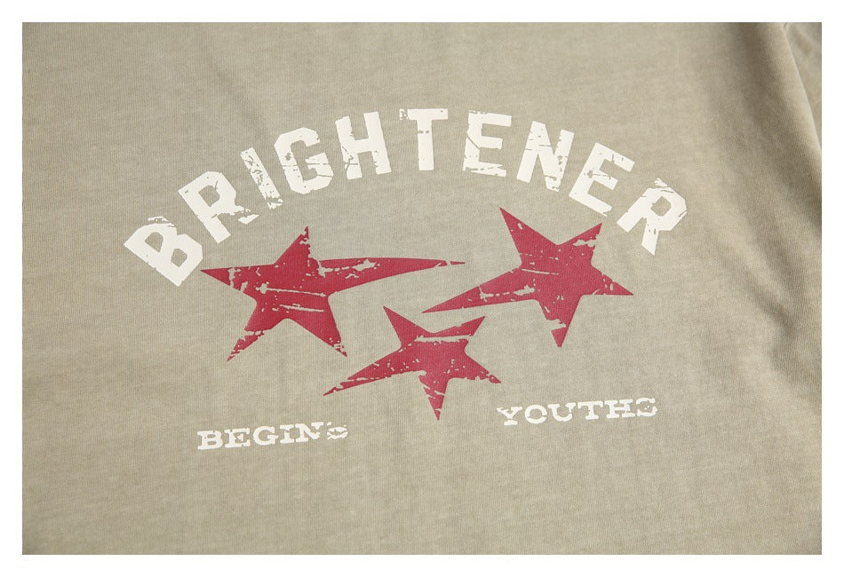 Close-up of the T-shirt's distressed white lettering and three red stars on sand-beige fabric.