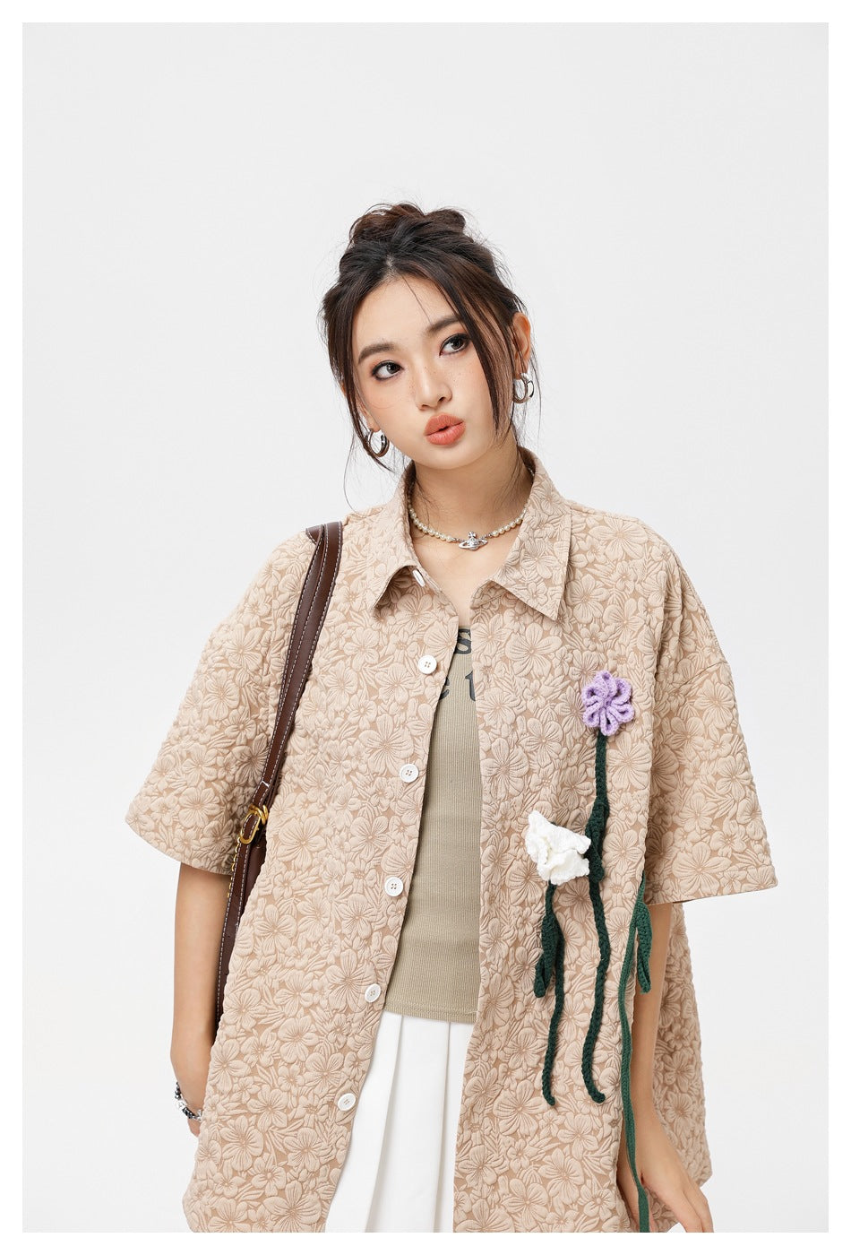 Upper-body view of a model wearing a beige floral-textured shirt with white buttons and purple and white flower appliqués.