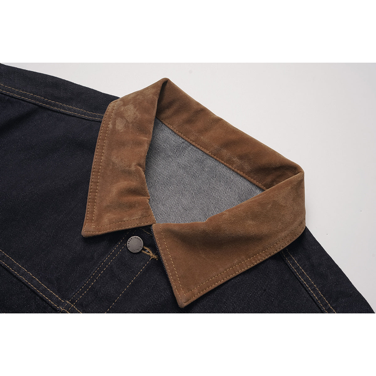 Close-up of a dark indigo jacket with a wide brown collar, striped underside, contrast stitching and a metal button.