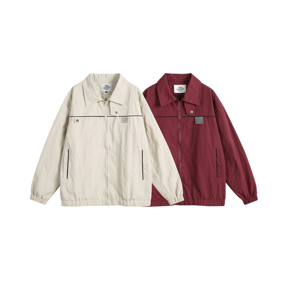 Two front-view zip jackets shown together: one ivory and one burgundy, both with black piping and chest patches.