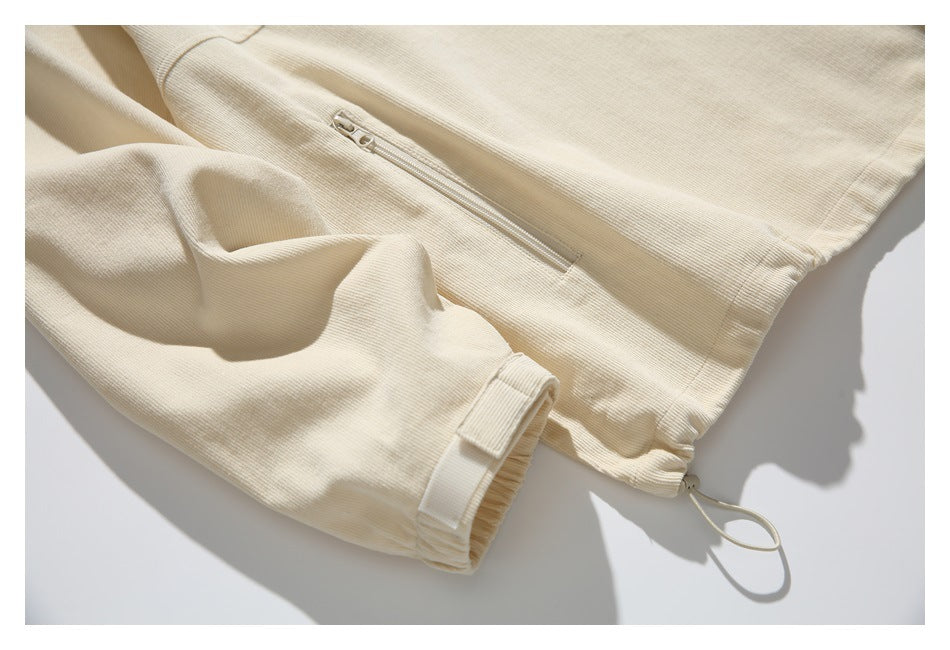 Close-up of a cream sleeve cuff and vertical zip pocket, with an adjustable loop at the hem.
