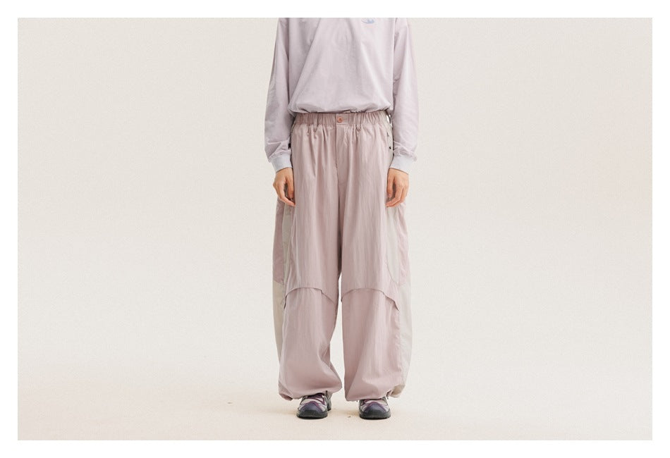 Front view of a model wearing pale lavender-pink loose pants with an elastic waist and curved knee panels.