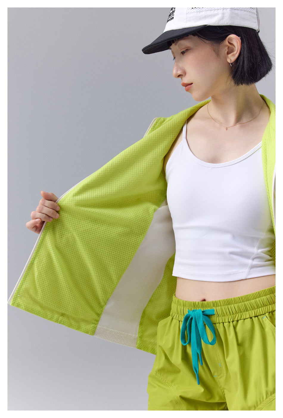 Model holding open the off-white jacket to show the neon yellow-green perforated mesh lining and side panel