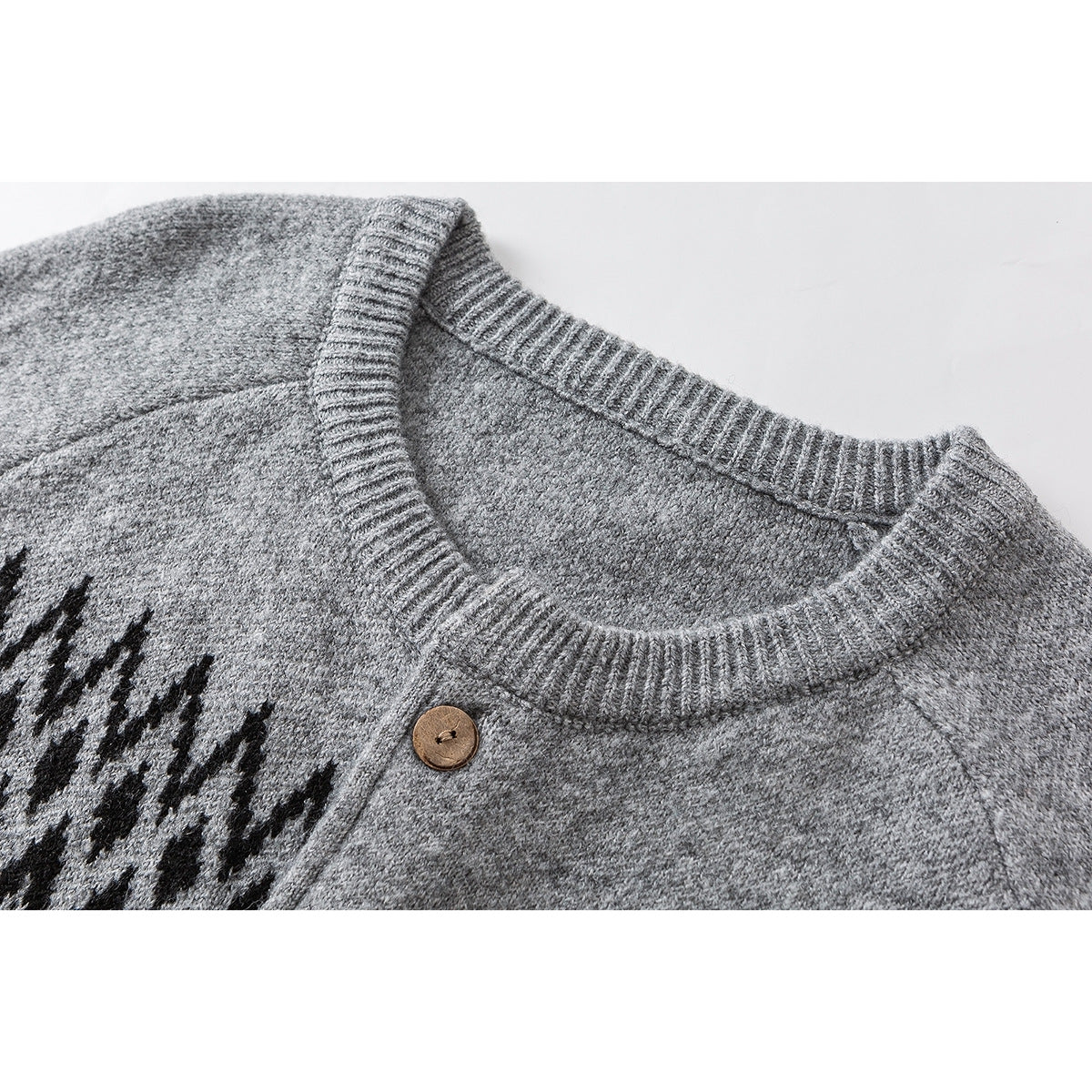 Close-up of a gray cardigan's ribbed crew neckline, wooden button, and black geometric knit pattern.