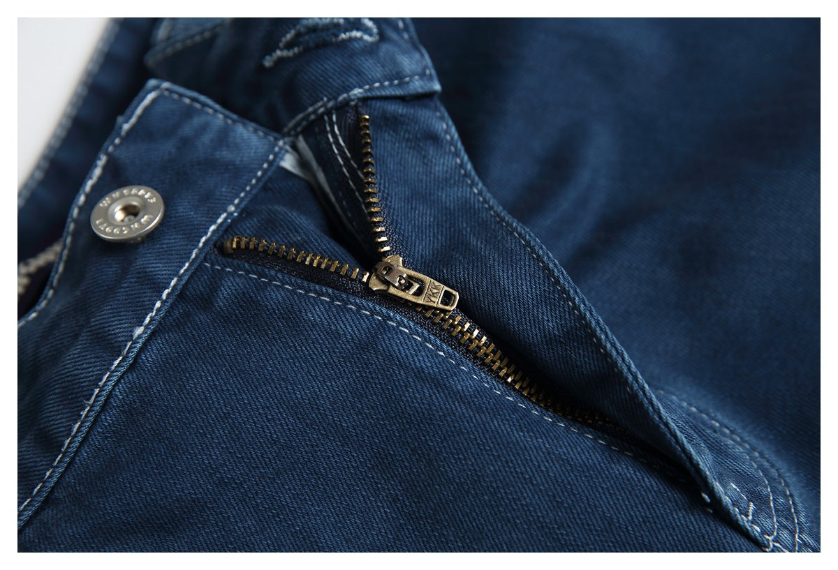 Close-up of dark blue jeans with the metal fly zipper partly open and the button visible.