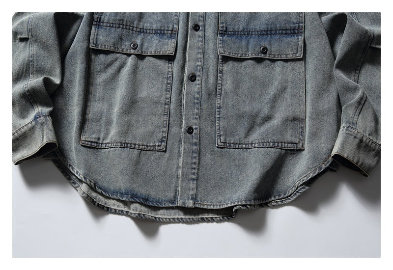 Close-up of the gray washed denim shirt’s lower front, showing two pockets, buttons and curved hem.