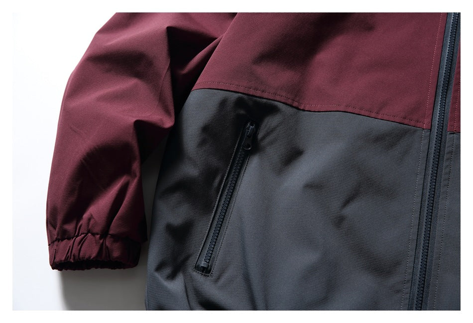 Close-up of a burgundy sleeve and charcoal jacket panel with an angled zip pocket.