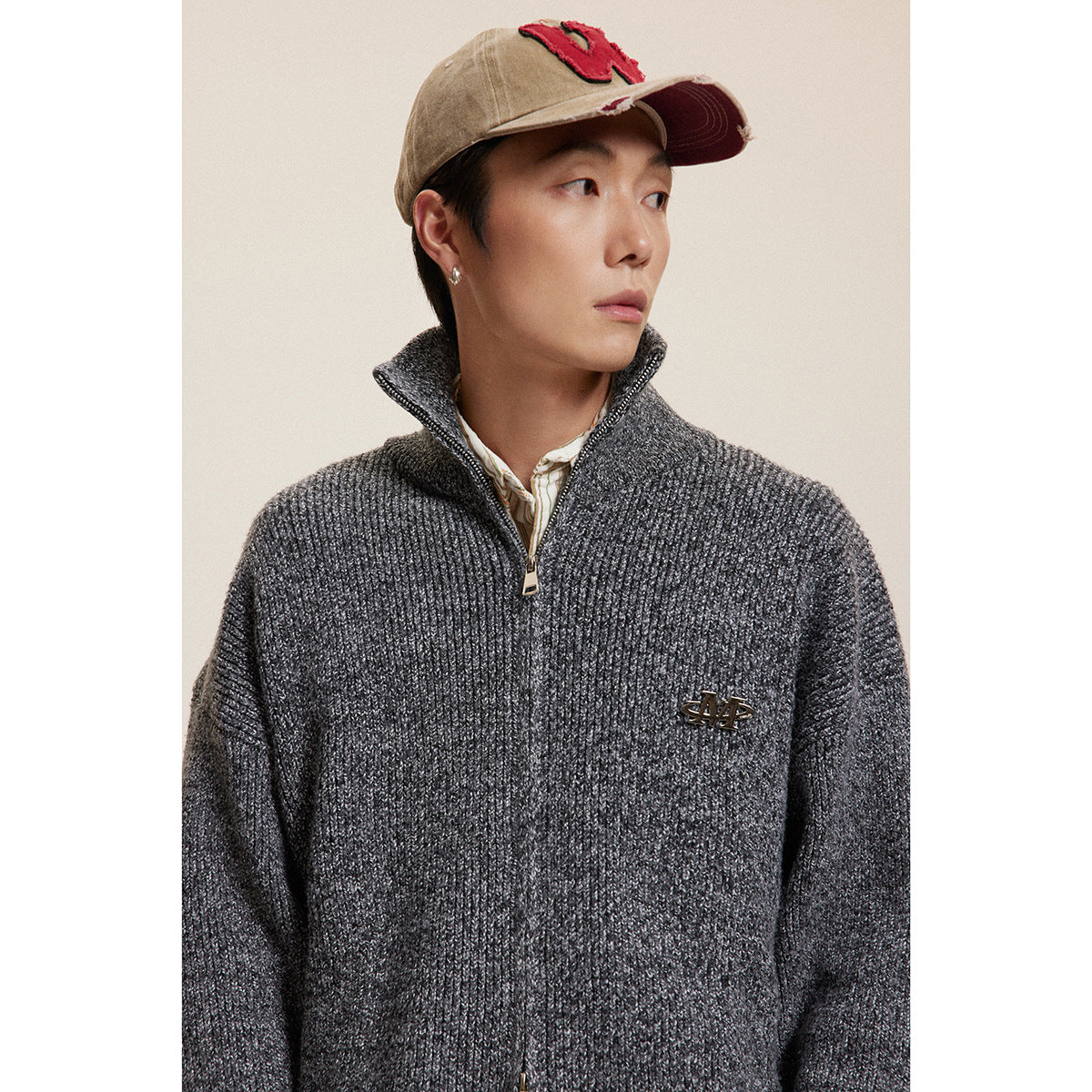Model wearing a charcoal ribbed zip-neck sweater with a raised collar and chest emblem.