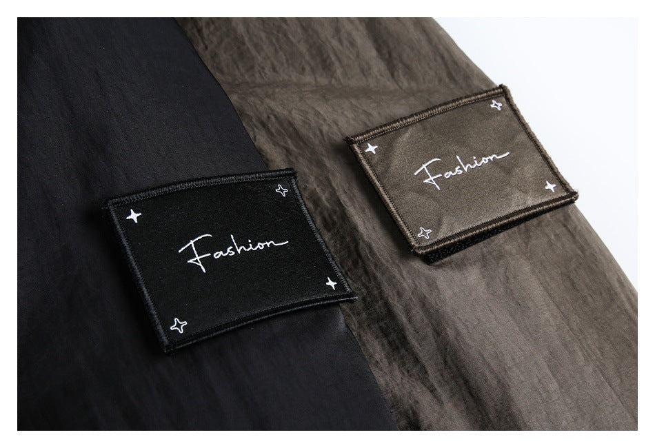 Close-up of black and dark brown coat fabric with rectangular embroidered Fashion patches and small stars.
