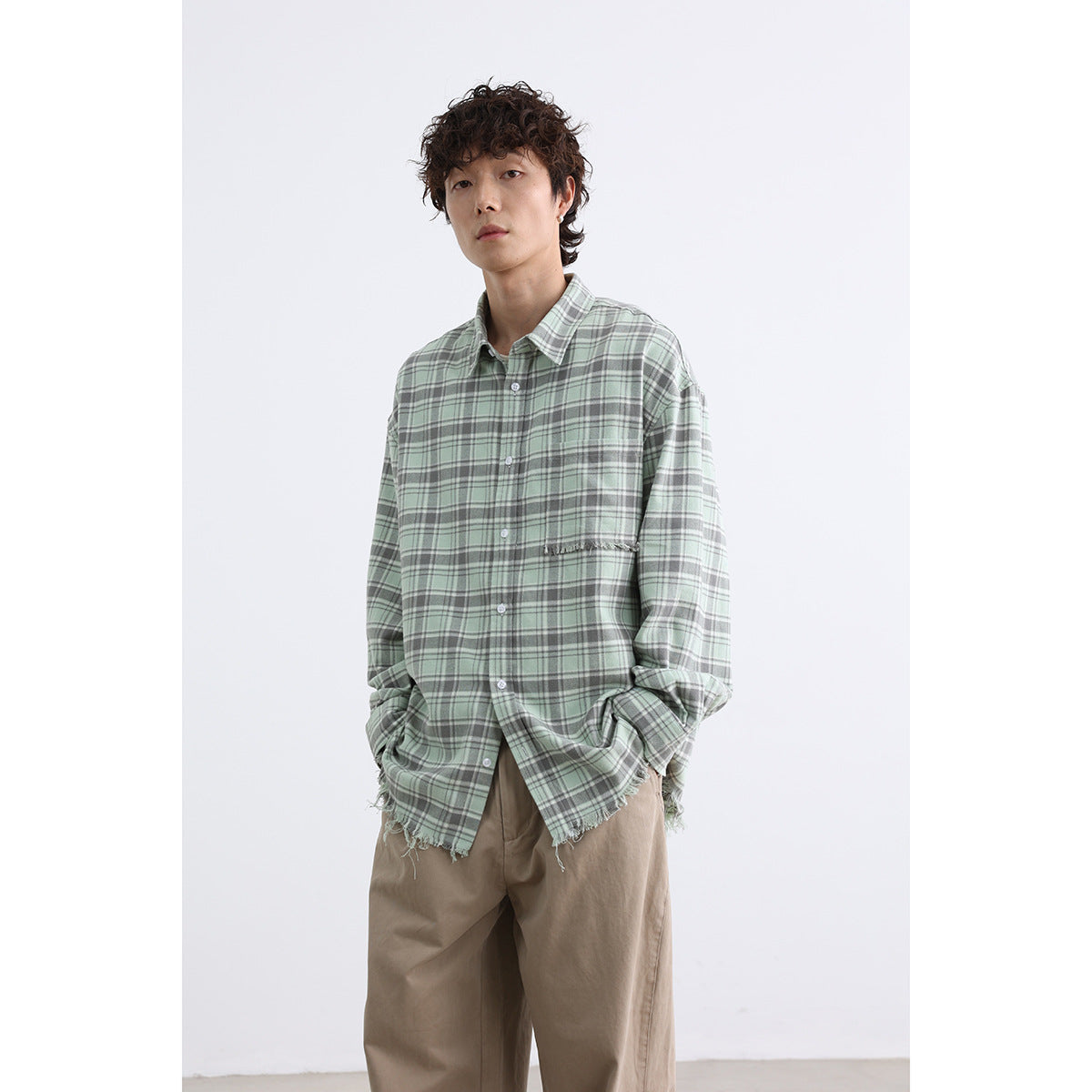 Model wearing an oversized sage green plaid button-up shirt with a chest pocket and frayed hem.