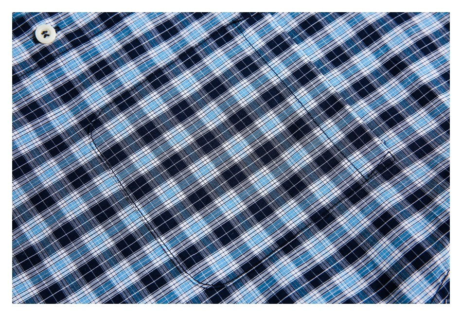 Close-up of a navy, light blue, and white plaid shirt showing a button and chest pocket stitching.