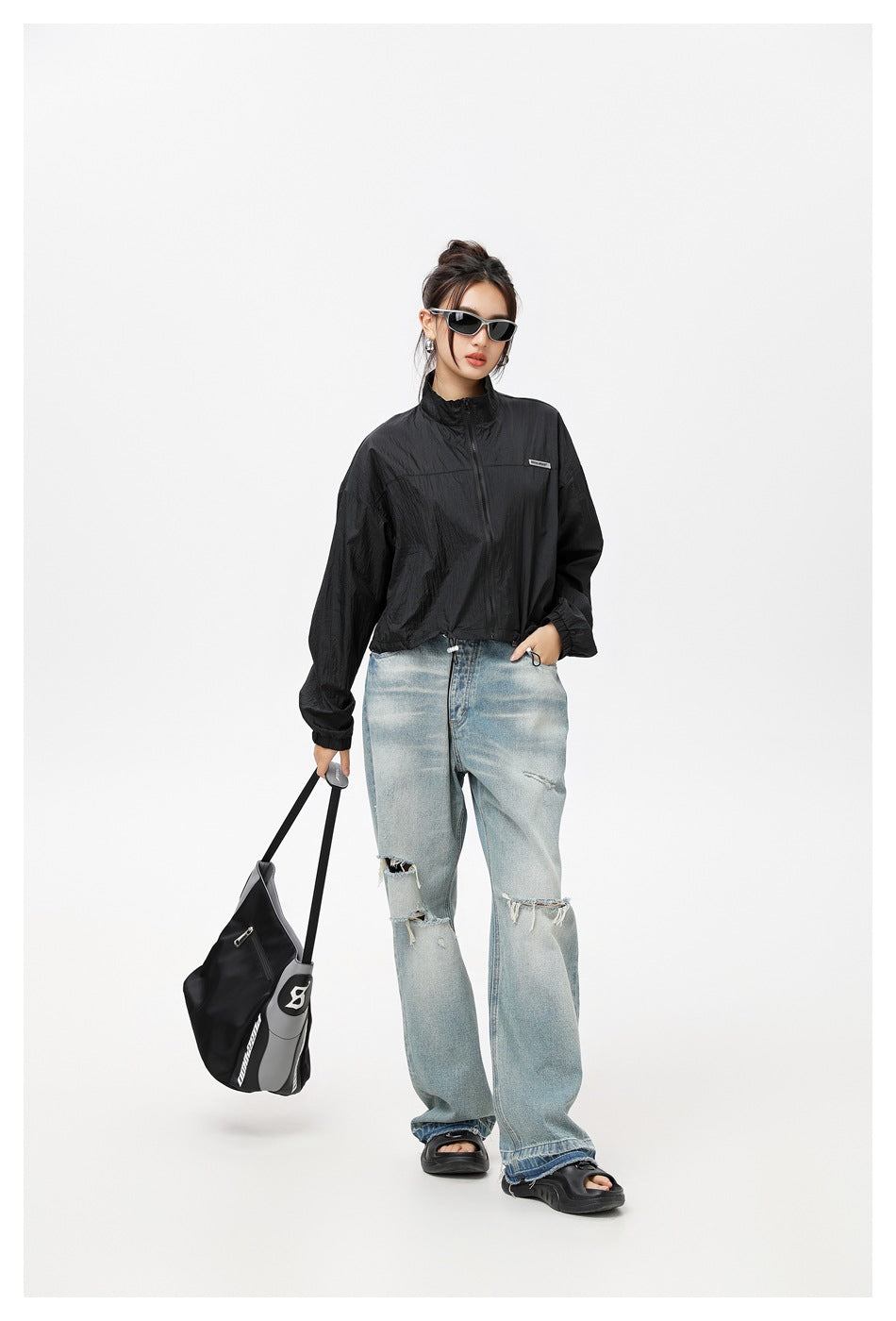 Model wearing a black cropped zip-up jacket with a high collar and light ripped jeans.