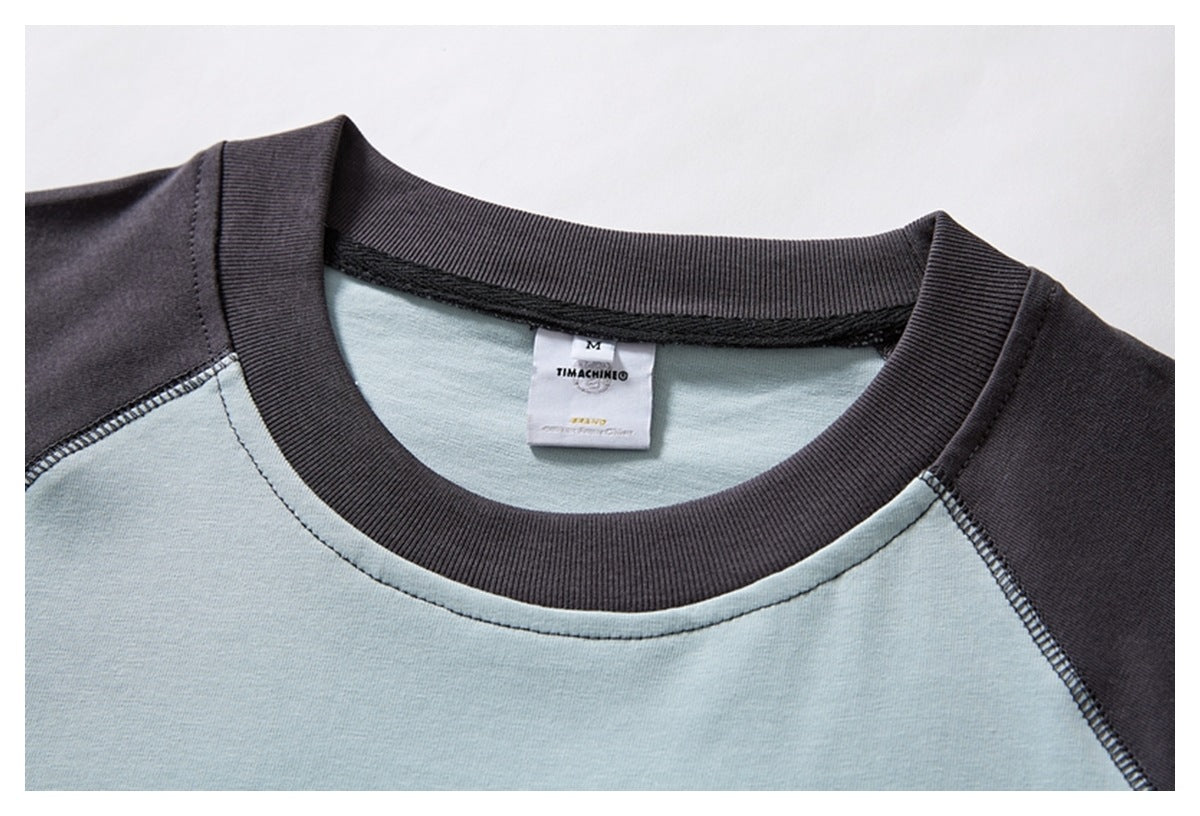 Close-up of a pale blue and charcoal raglan T-shirt neckline, ribbed collar, seams, and sewn neck label.
