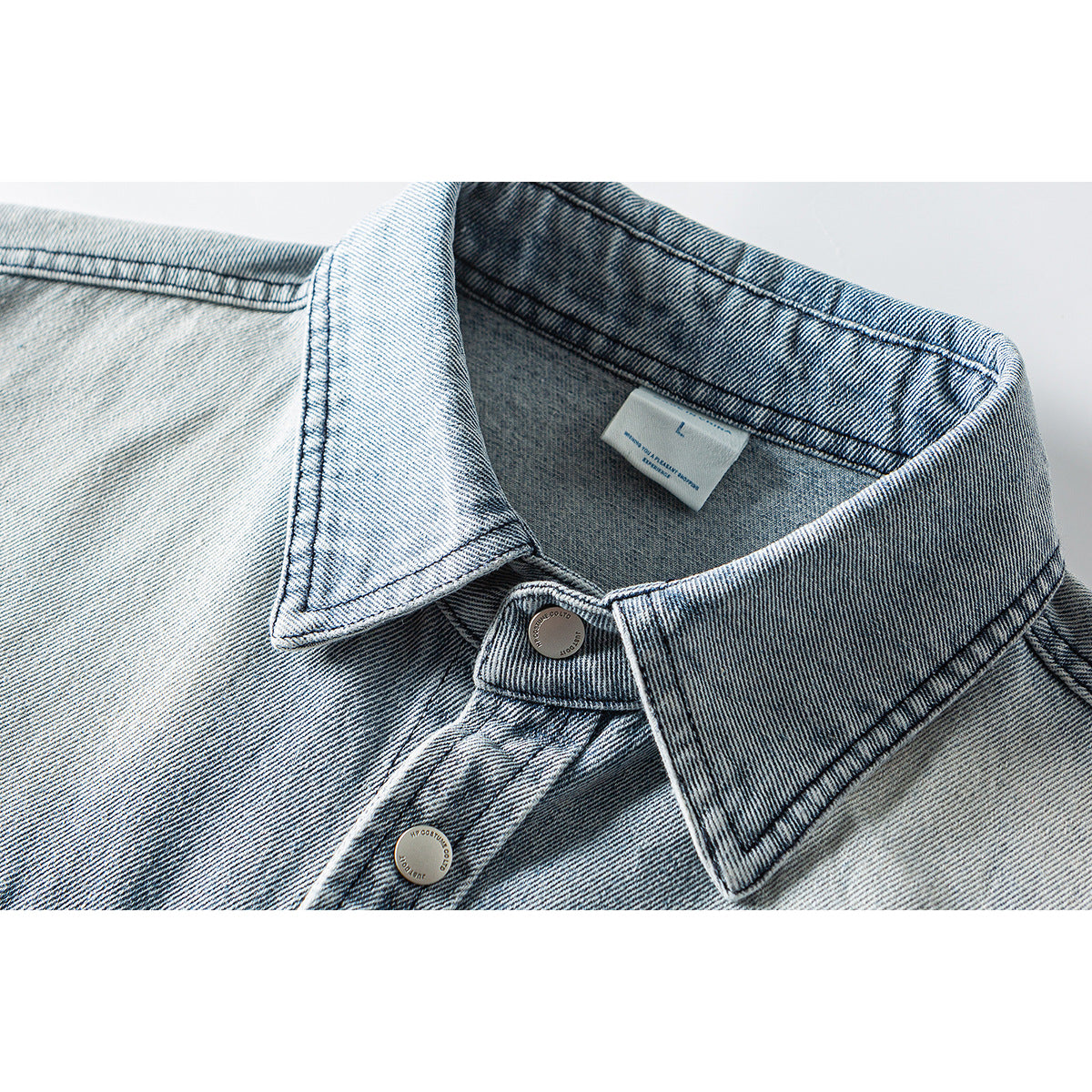 Close-up of a light blue denim jacket collar, inner label, and metal buttons.