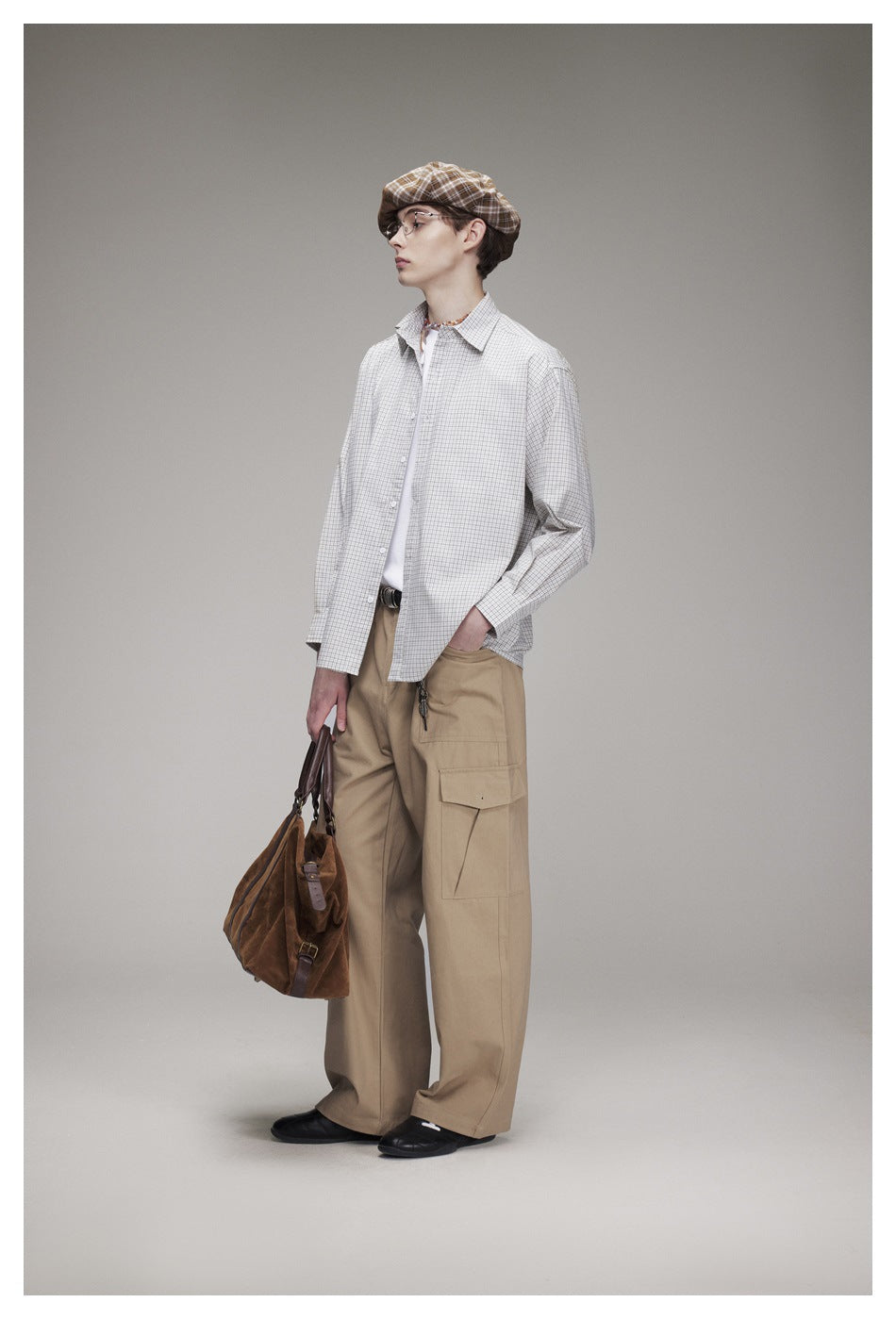 Full-length model wearing an oversized light gray checked shirt, tan cargo trousers, a brown plaid cap, and black shoes.