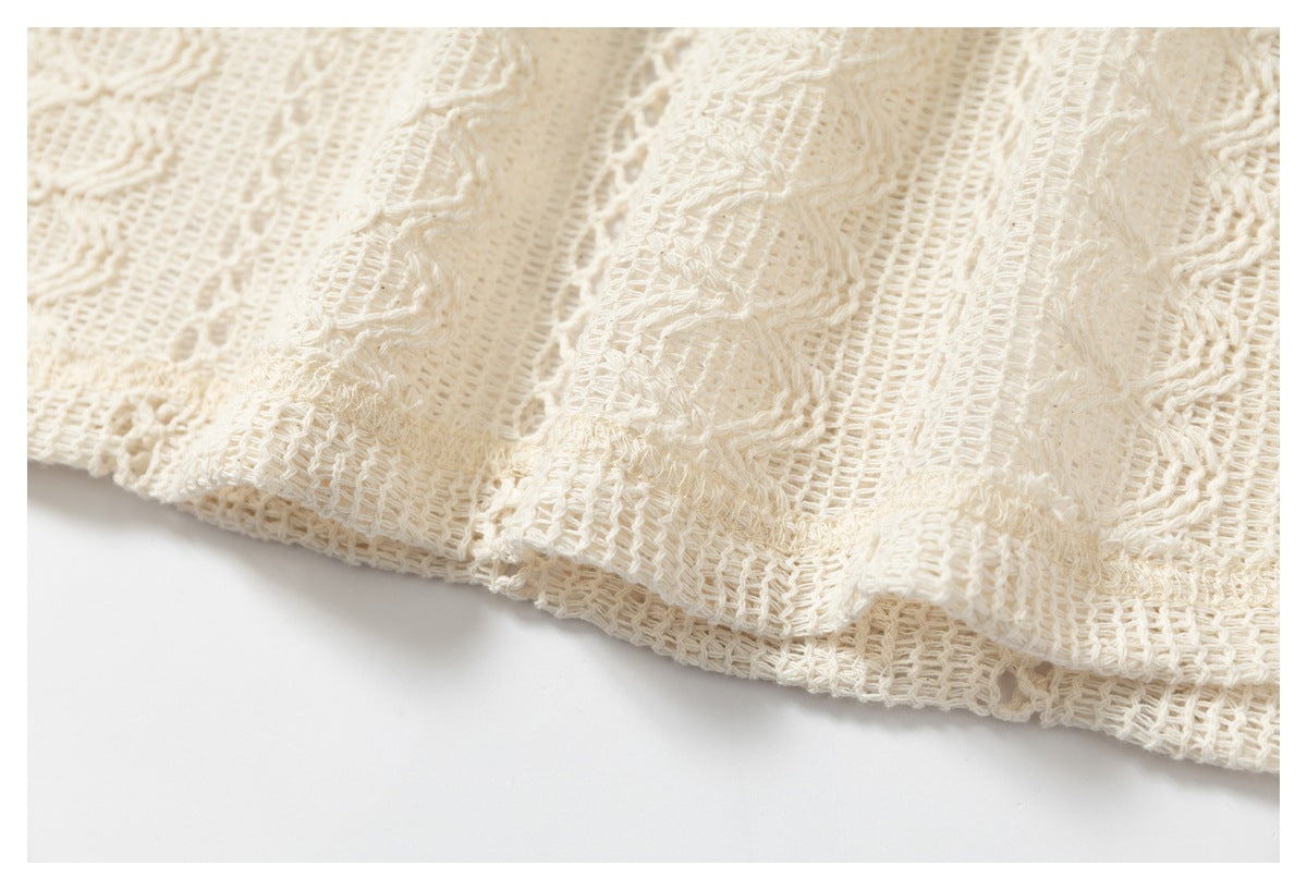 Close-up of a cream open-knit garment's patterned fabric and hem edge.