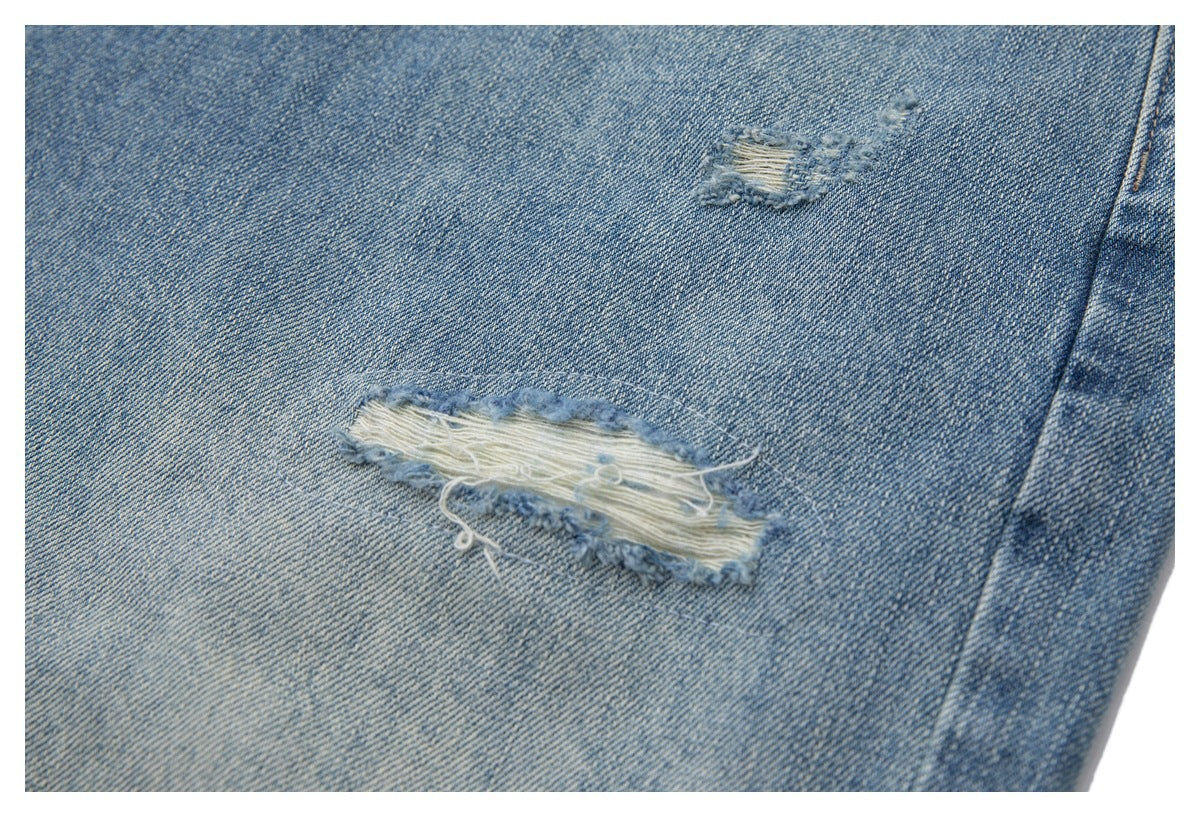 Close-up of light blue denim with two distressed frayed patches.