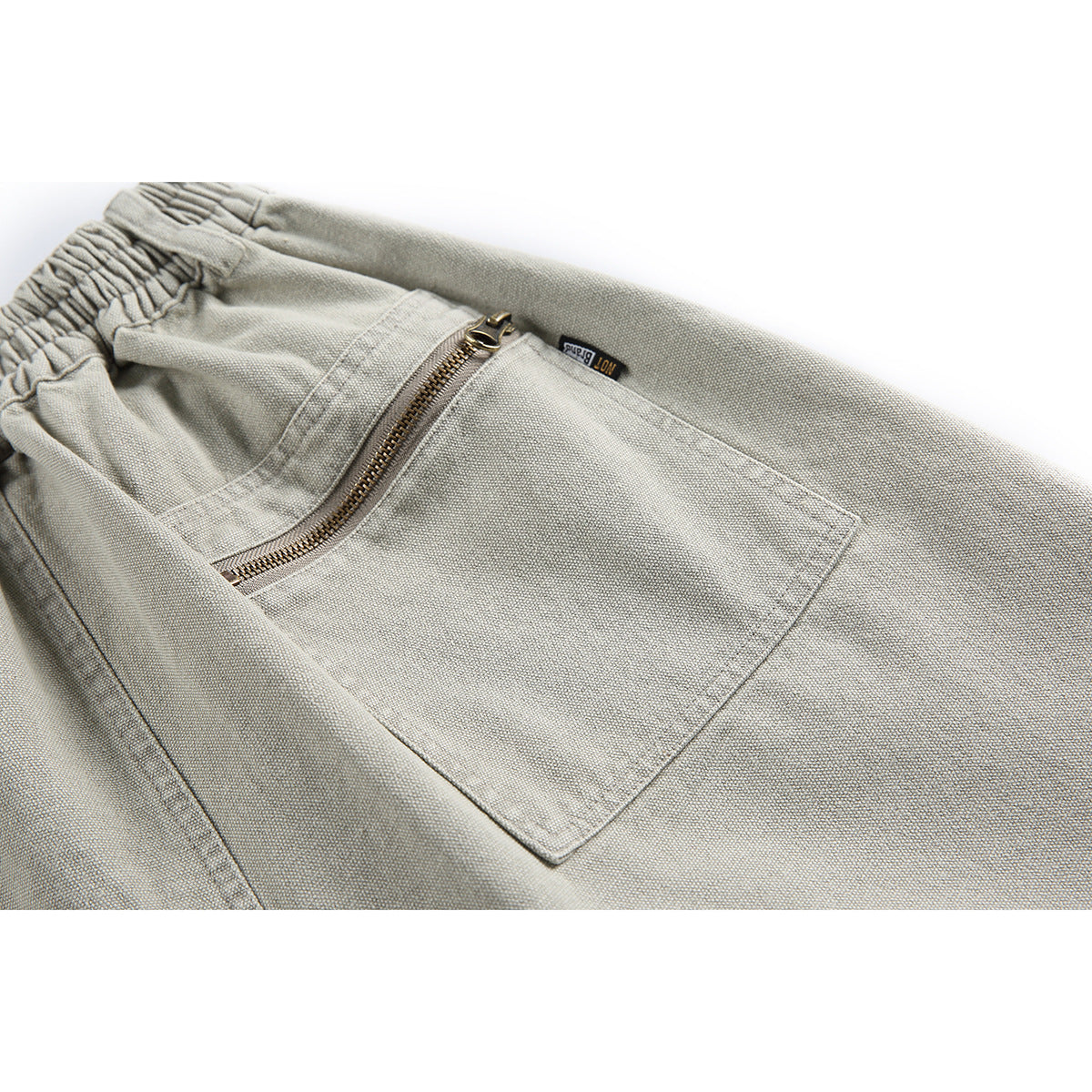 Close-up of light gray shorts showing an elastic waistband and a large zippered pocket.