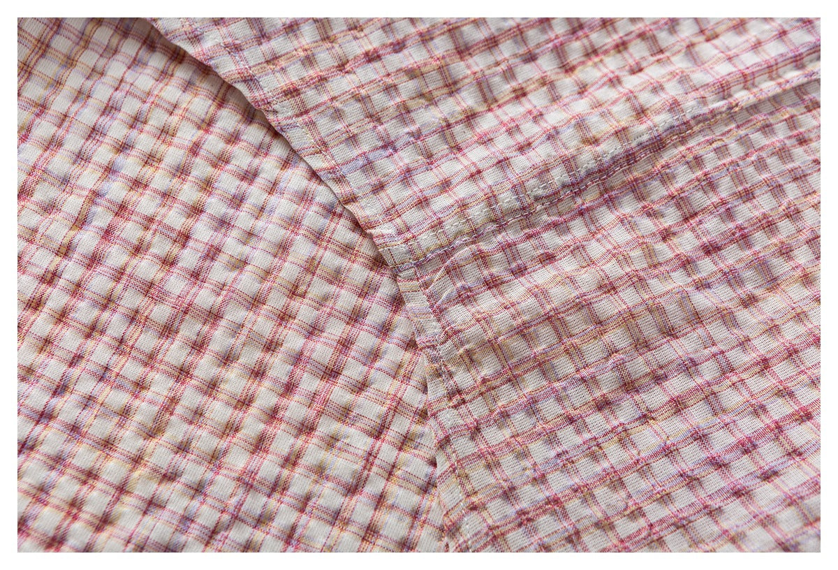 Close-up of cream fabric with a pink, red, and muted yellow plaid pattern and a diagonal stitched seam.