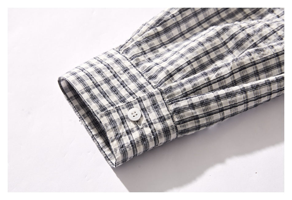 Close-up of a buttoned cuff on a cream shirt with a black and gray plaid pattern.