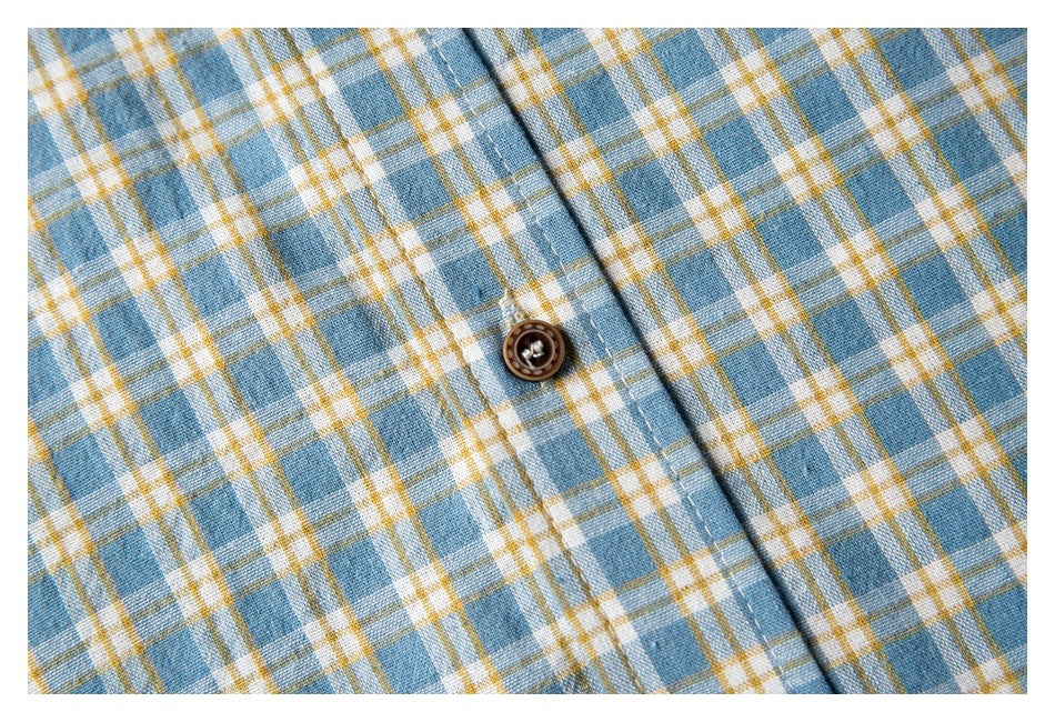 Close-up of a brown button and stitching on the shirt's blue, white, and mustard plaid fabric.