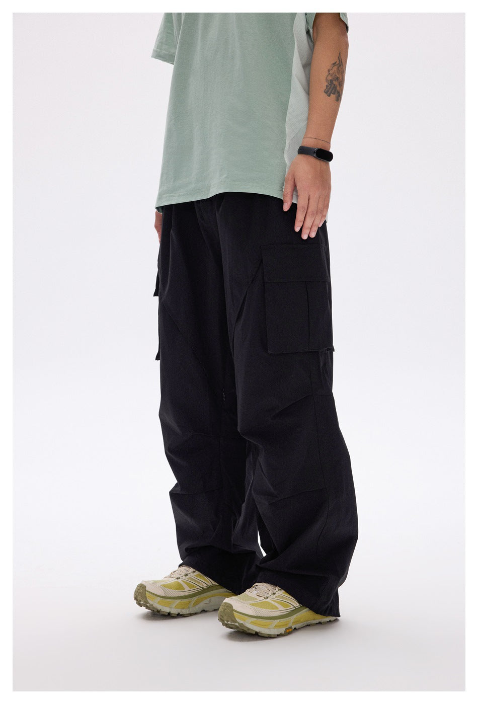 Side view of a model wearing loose black cargo pants with a large layered thigh pocket and angular panel seams.