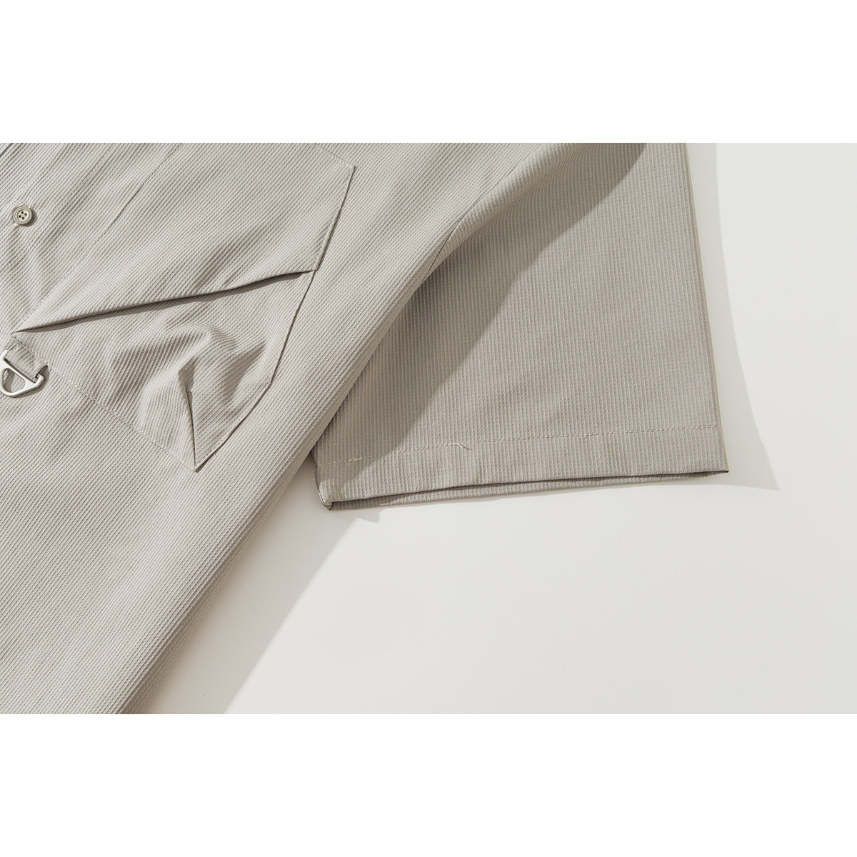Close-up of the light gray shirt’s chest pocket and short sleeve with fine textured fabric.