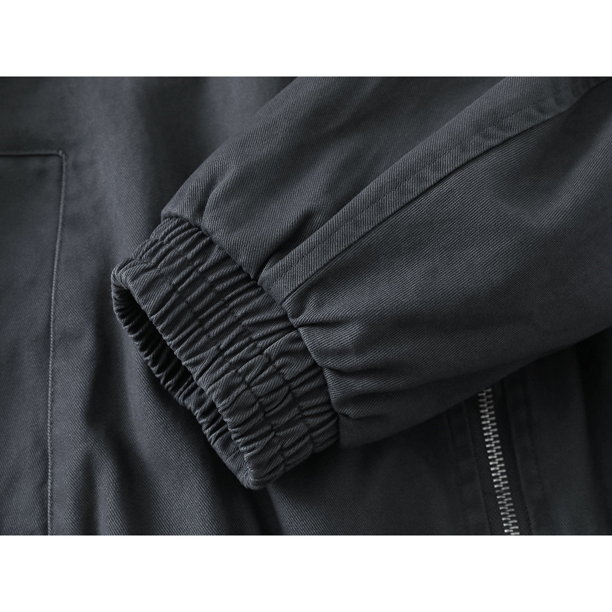 Close-up of a charcoal jacket sleeve and gathered elastic cuff, with part of the zipper and pocket visible.