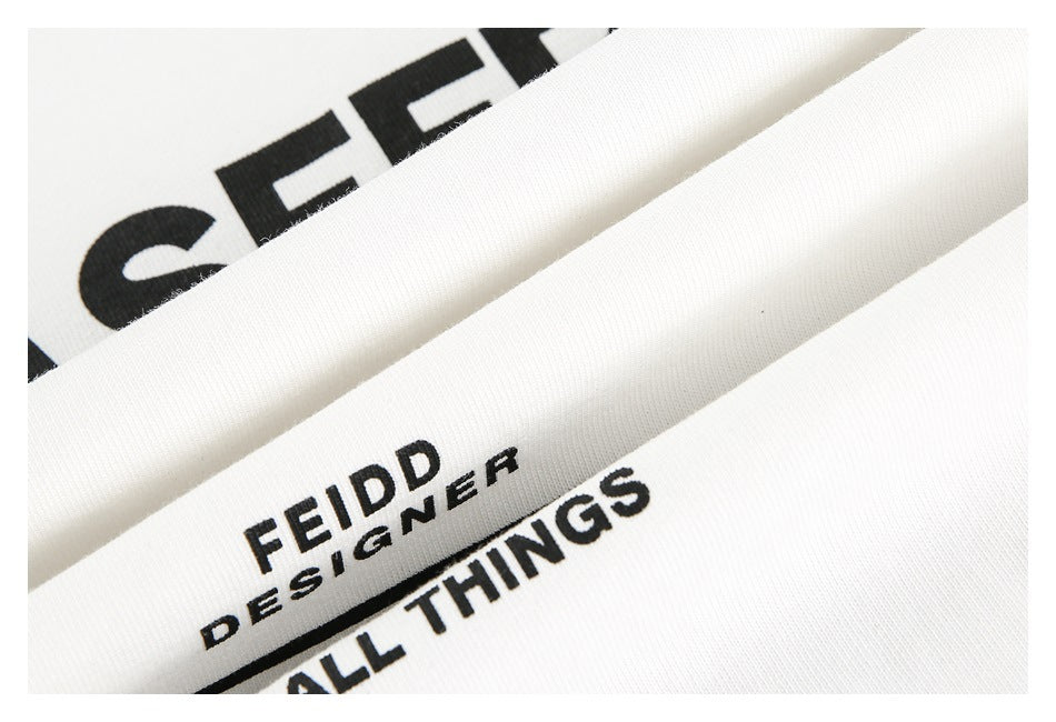 White garment close-up showing black printed lettering and a smaller FEIDD DESIGNER print.