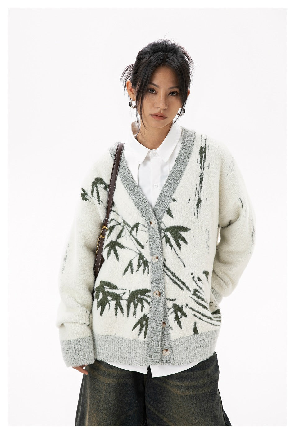 Front view of a model wearing an ivory button-front cardigan with gray ribbed trim and dark green botanical motifs.