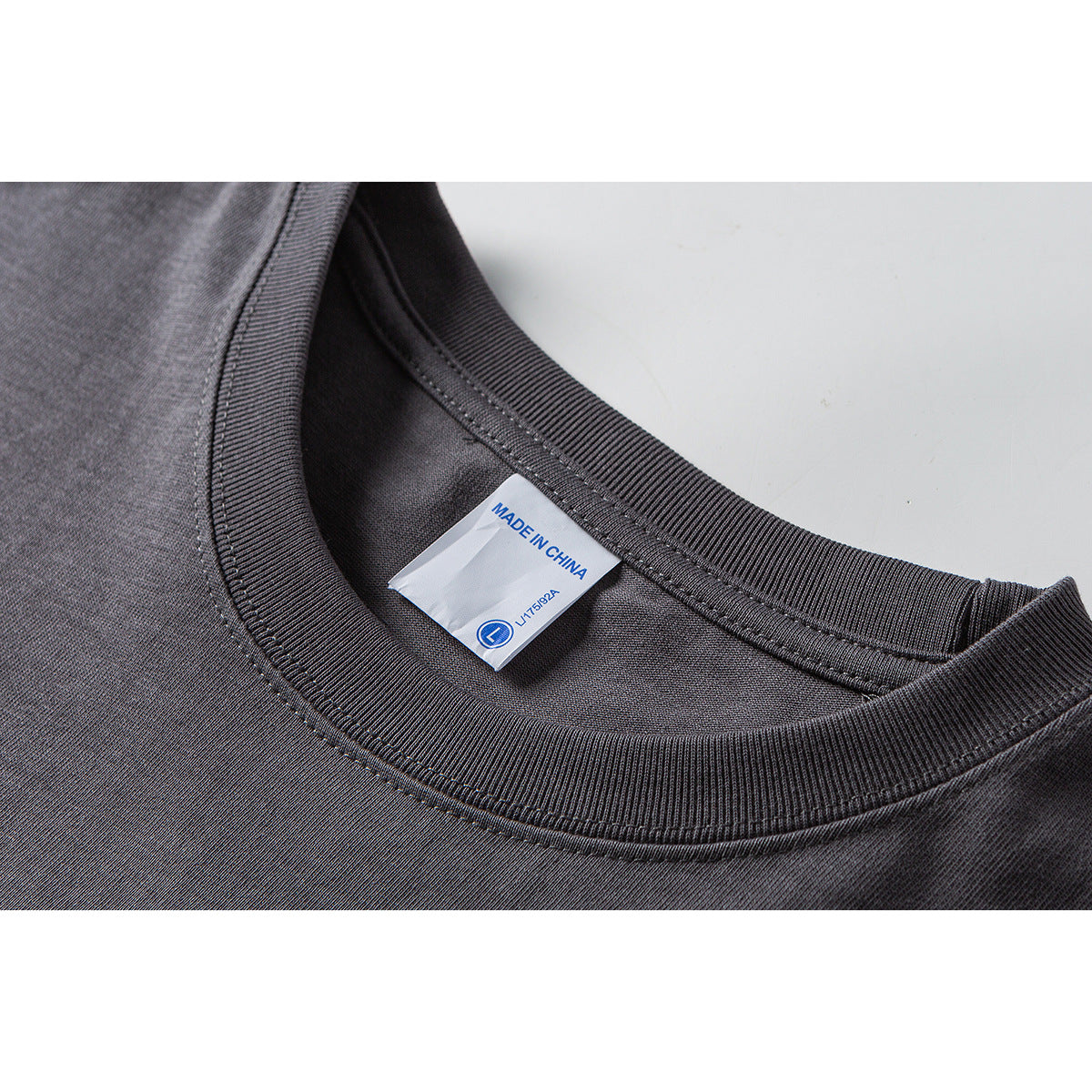 Close-up of a charcoal T-shirt's ribbed crew neckline and sewn label reading “MADE IN CHINA.”