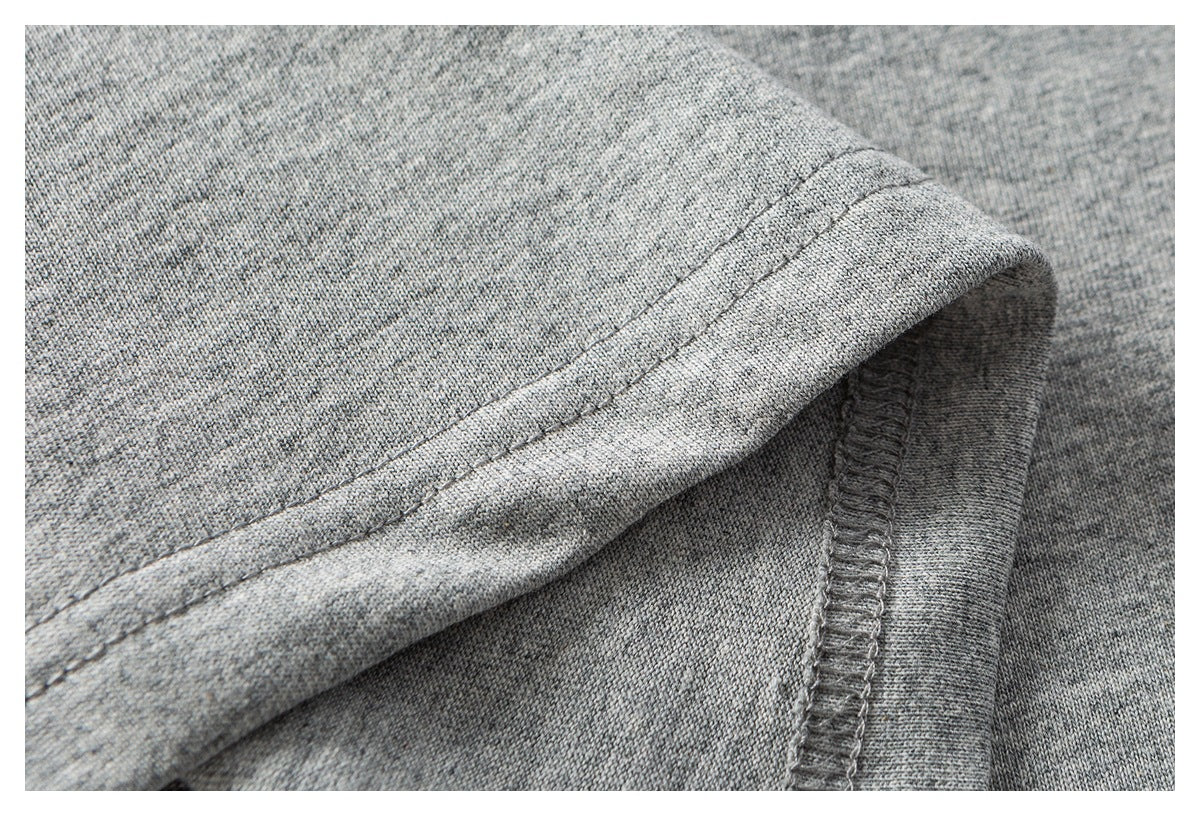 Close-up of heather gray knit fabric with a folded double-stitched hem and an overlocked seam.