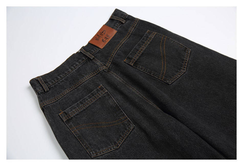 Dark charcoal jeans laid flat, viewed from the back with two stitched pockets and a brown waistband patch.