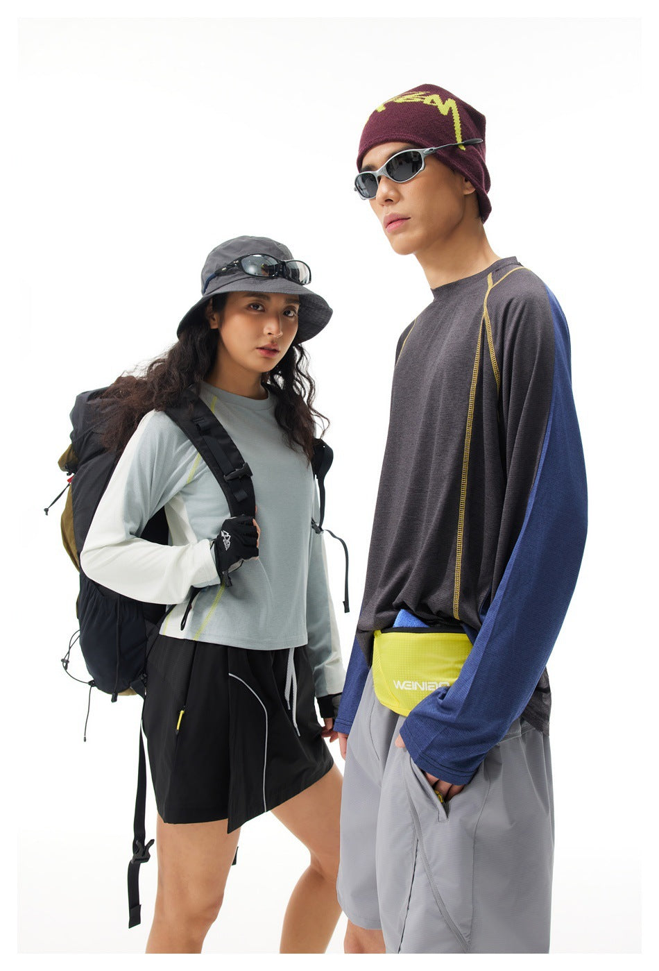 Two models in outdoor outfits: a woman in a pale blue long-sleeve top and black skirt, and a man in a charcoal top and gray