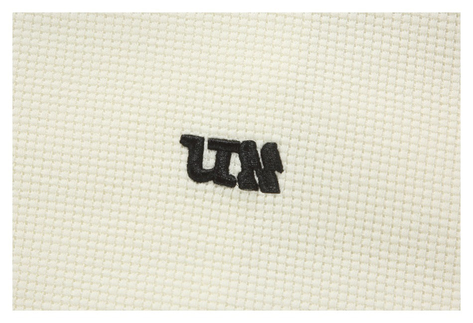 Close-up of a small black embroidered emblem on cream textured fabric.