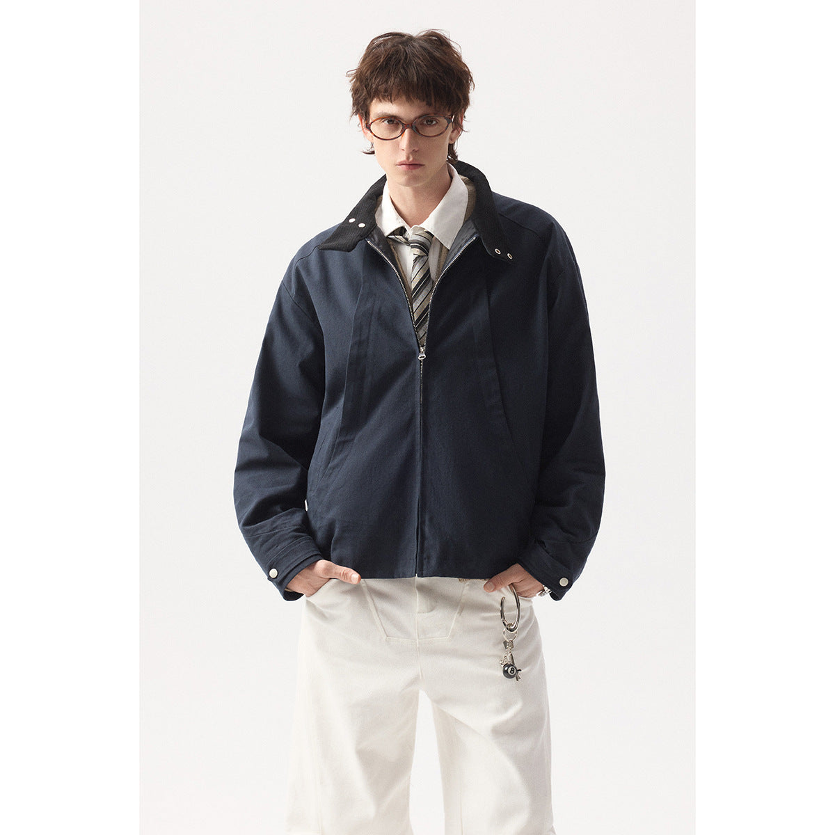Model wearing a dark navy zip-front jacket with a contrasting collar and snap cuffs, styled with white trousers.