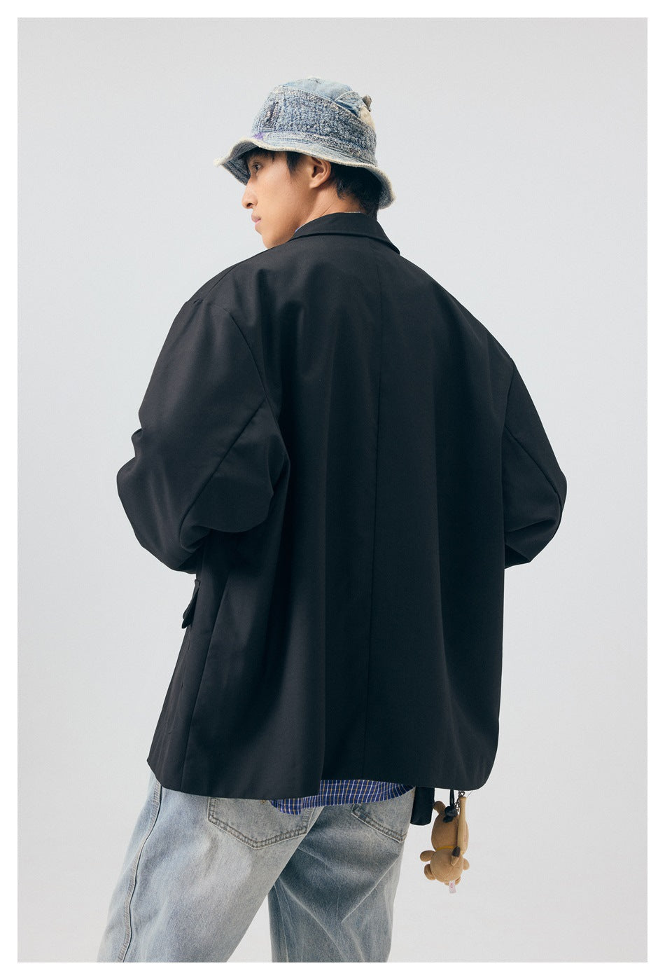 Rear view of a person wearing an oversized black blazer, light-wash jeans and a blue-gray bucket hat.