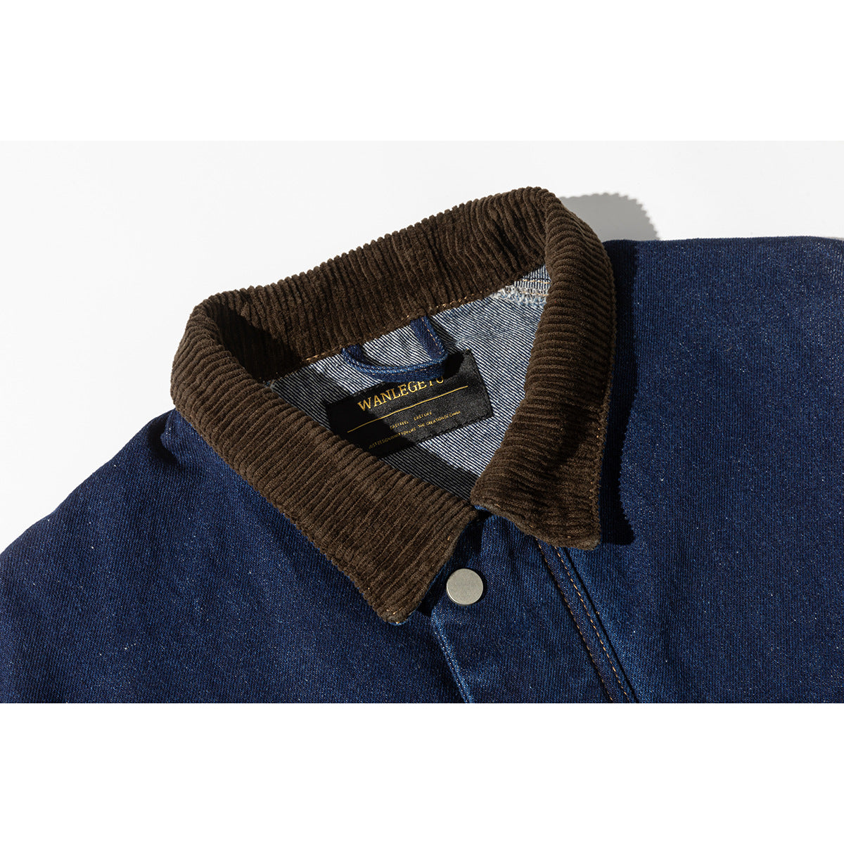 Close-up of a dark blue denim jacket with a brown corduroy collar, metal snap, and sewn-in neck label.
