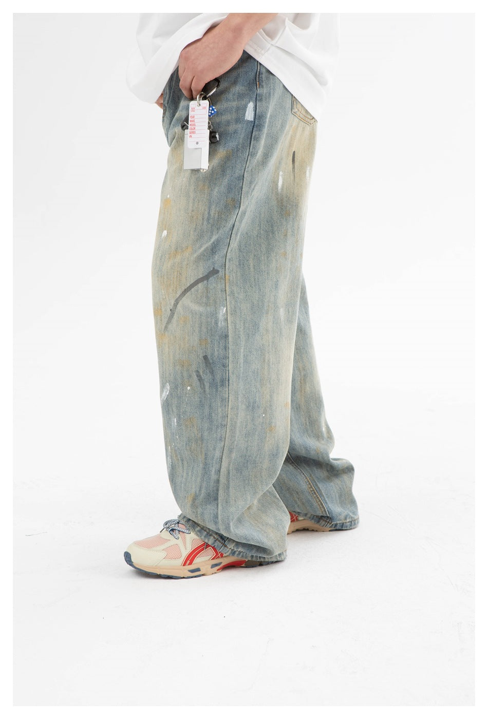 Side view of a model wearing wide faded blue jeans with scattered paint-like marks and a hanging tag.