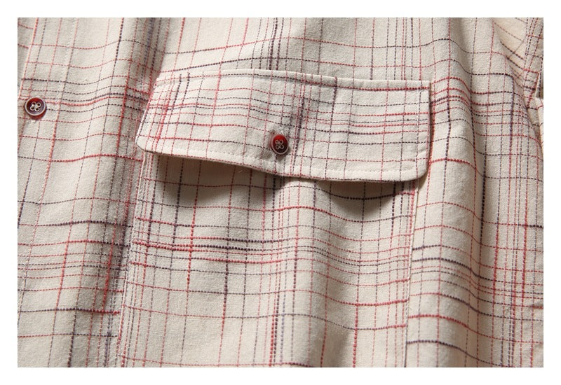 Close-up of a beige plaid shirt pocket flap with dark buttons and red and gray checks.