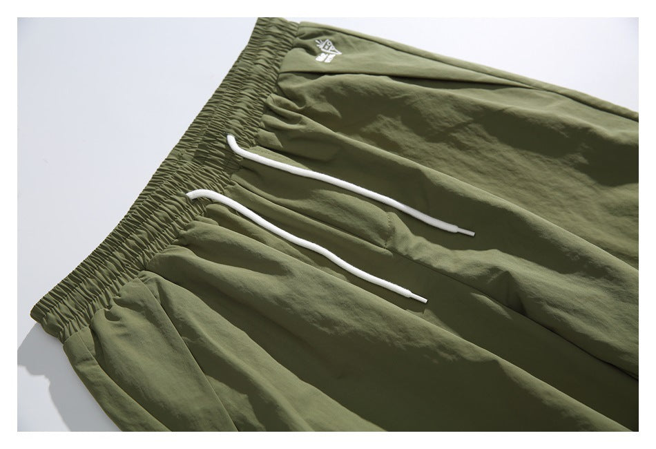 Close-up of olive green pants showing the elastic waistband, white drawstrings, and small garment emblem.
