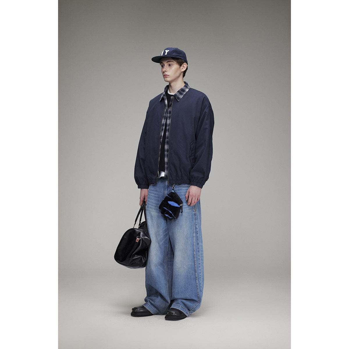Full-length view of a model wearing a navy jacket with plaid trim and loose light-wash jeans.