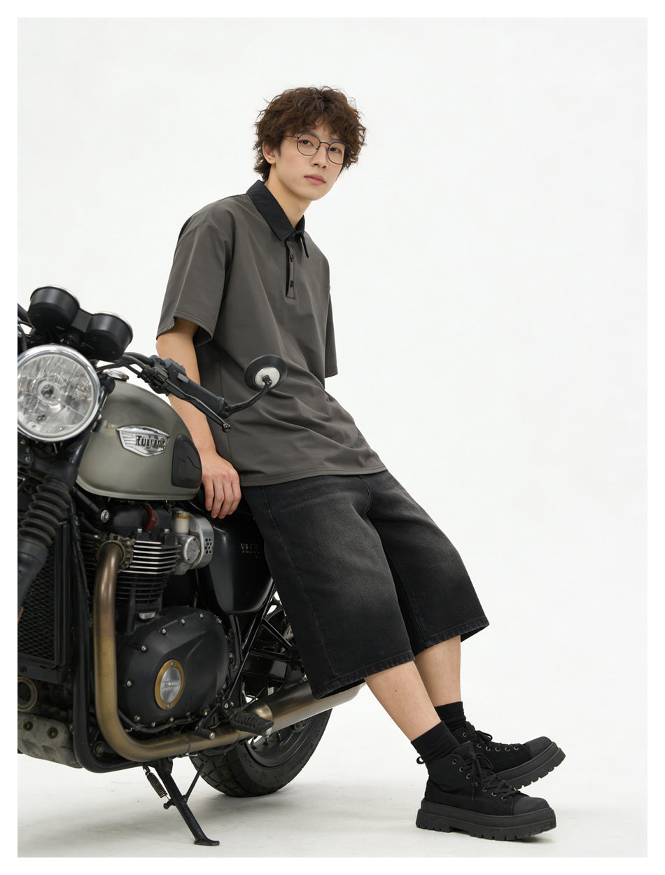 Model in the dark gray polo-style top and black denim shorts leaning on a motorcycle in a studio