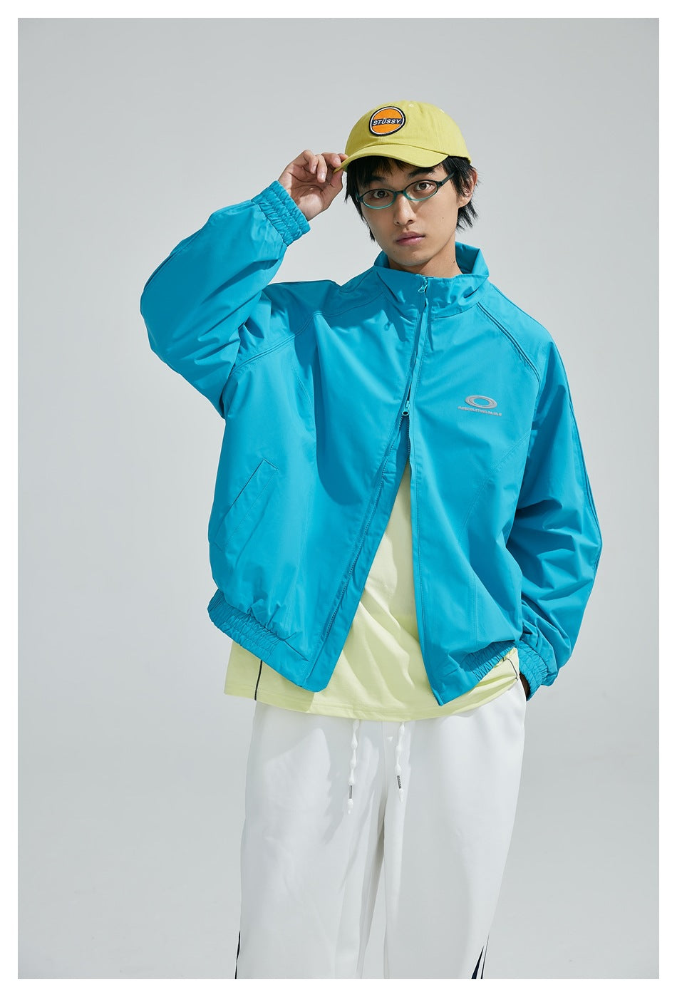 Model wearing a turquoise zip-up jacket over a pale yellow shirt, shown from the front.